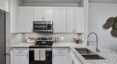 Luxury kitchen with white cabinets, granite countertops, and stainless steel appliances at our apartments on Parker Road